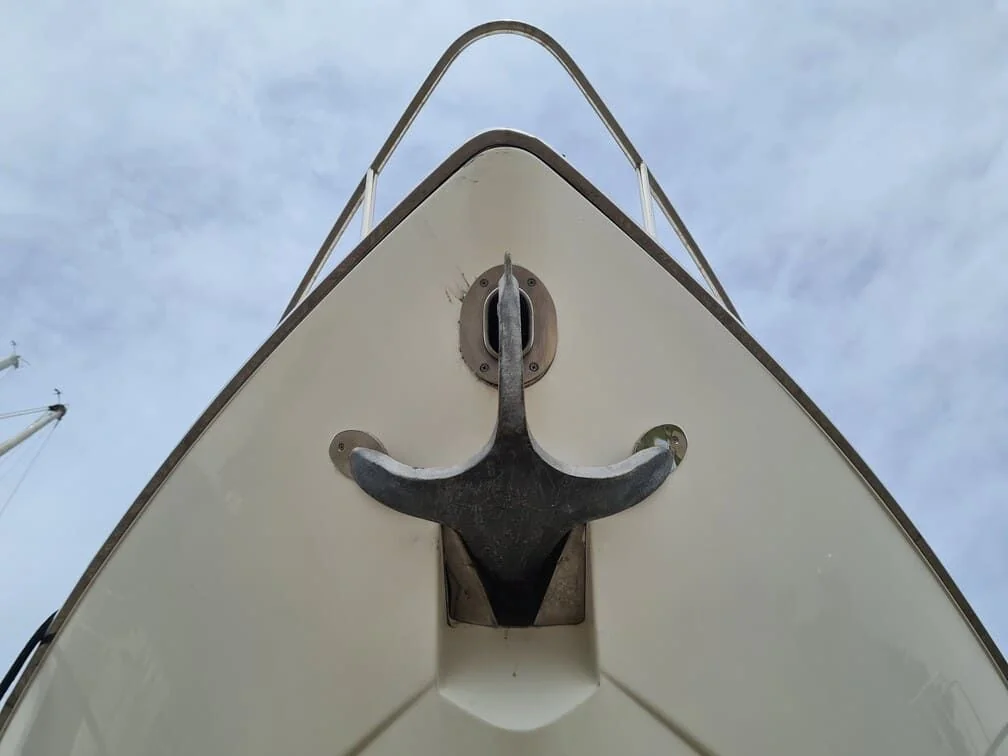 Boat bow anchor and cleat hardware showing weathered patina against cream hull.