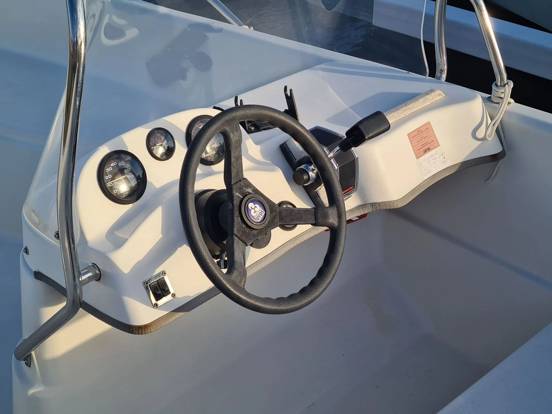 Boat console dashboard with steering wheel and gauges in bright sunlight.