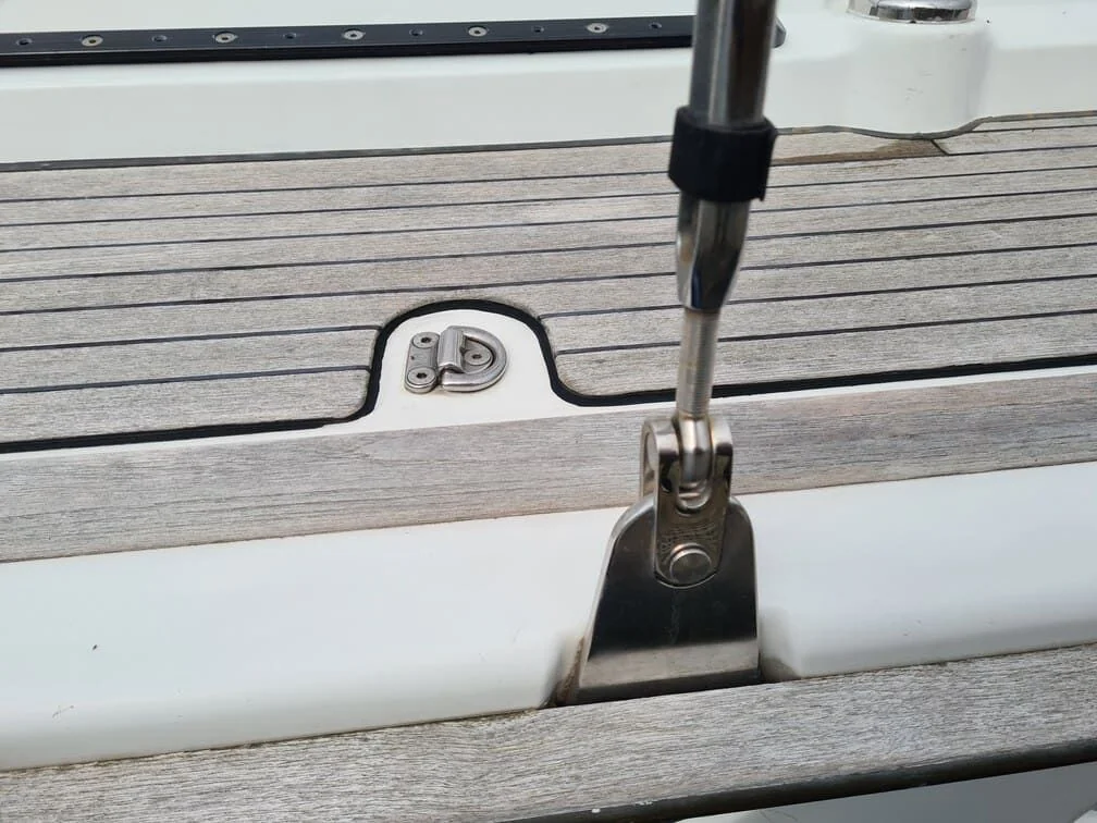 Close-up of boat deck hardware and stainless steel cleat with weathered teak rail.