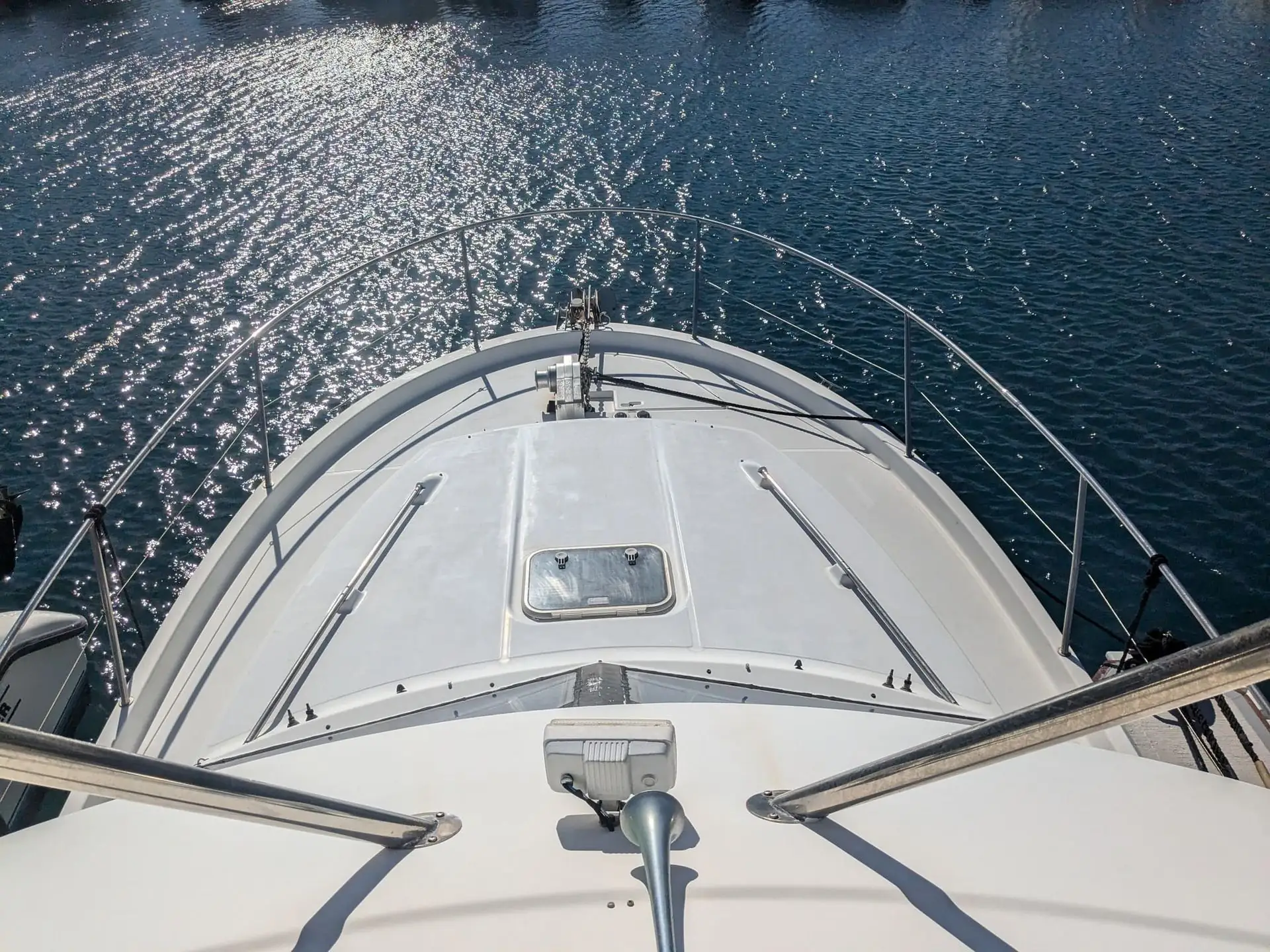 Fiberglass motorboat bow viewed from above, docked with calm water and bright sunlight reflecting off surface.