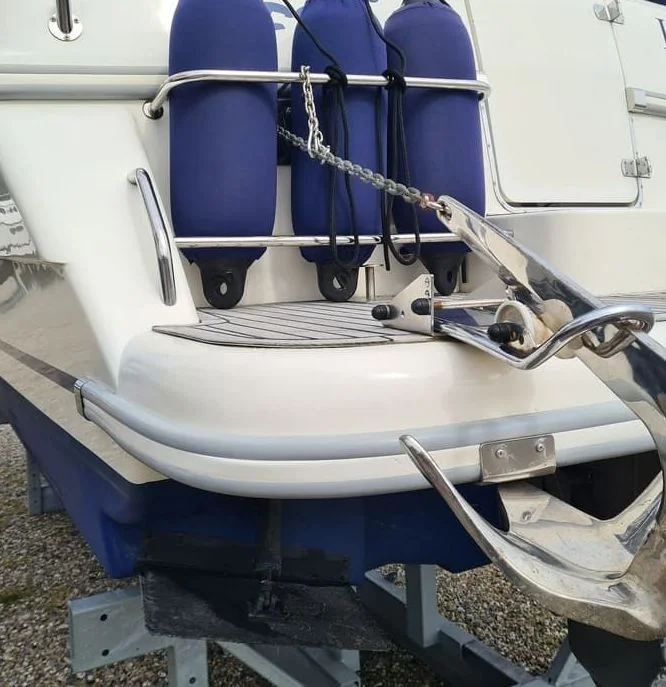 Boat transom with three blue fenders secured by rail and rope, mounted on trailer.