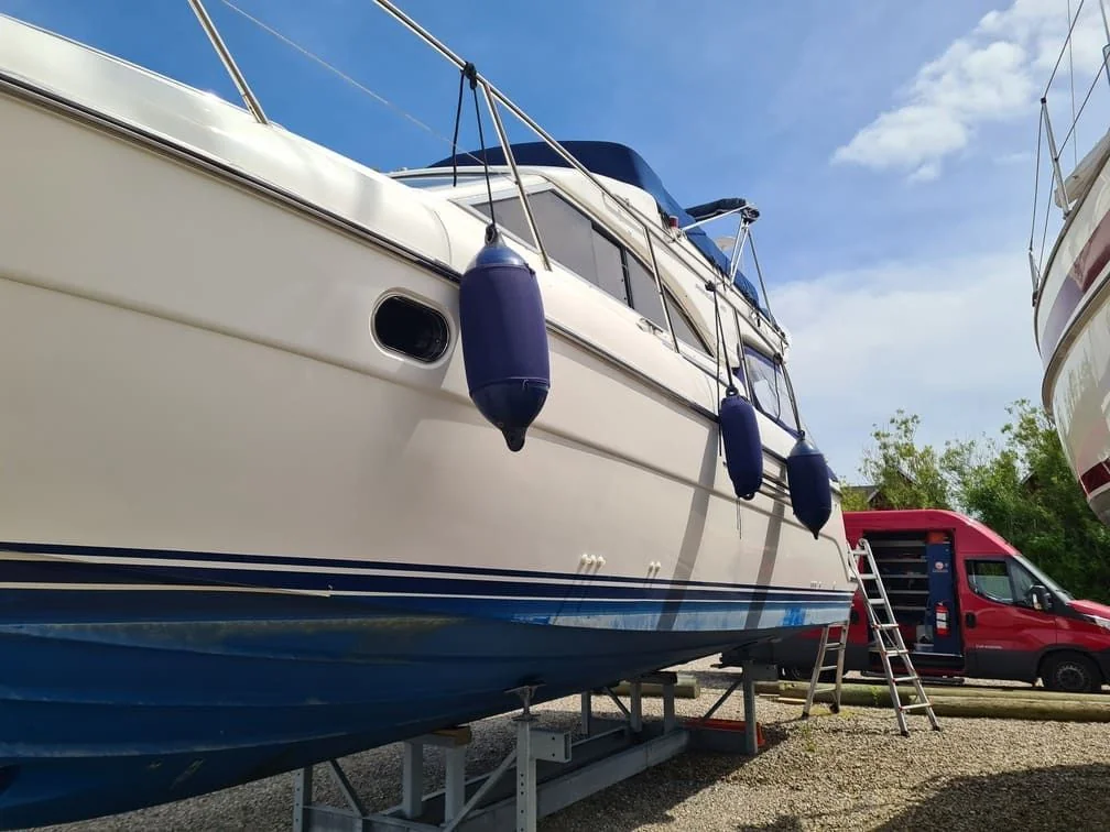 Fiberglass motorboat on dry dock with blue hull stripe and white cabin, service ladder positioned for access.
