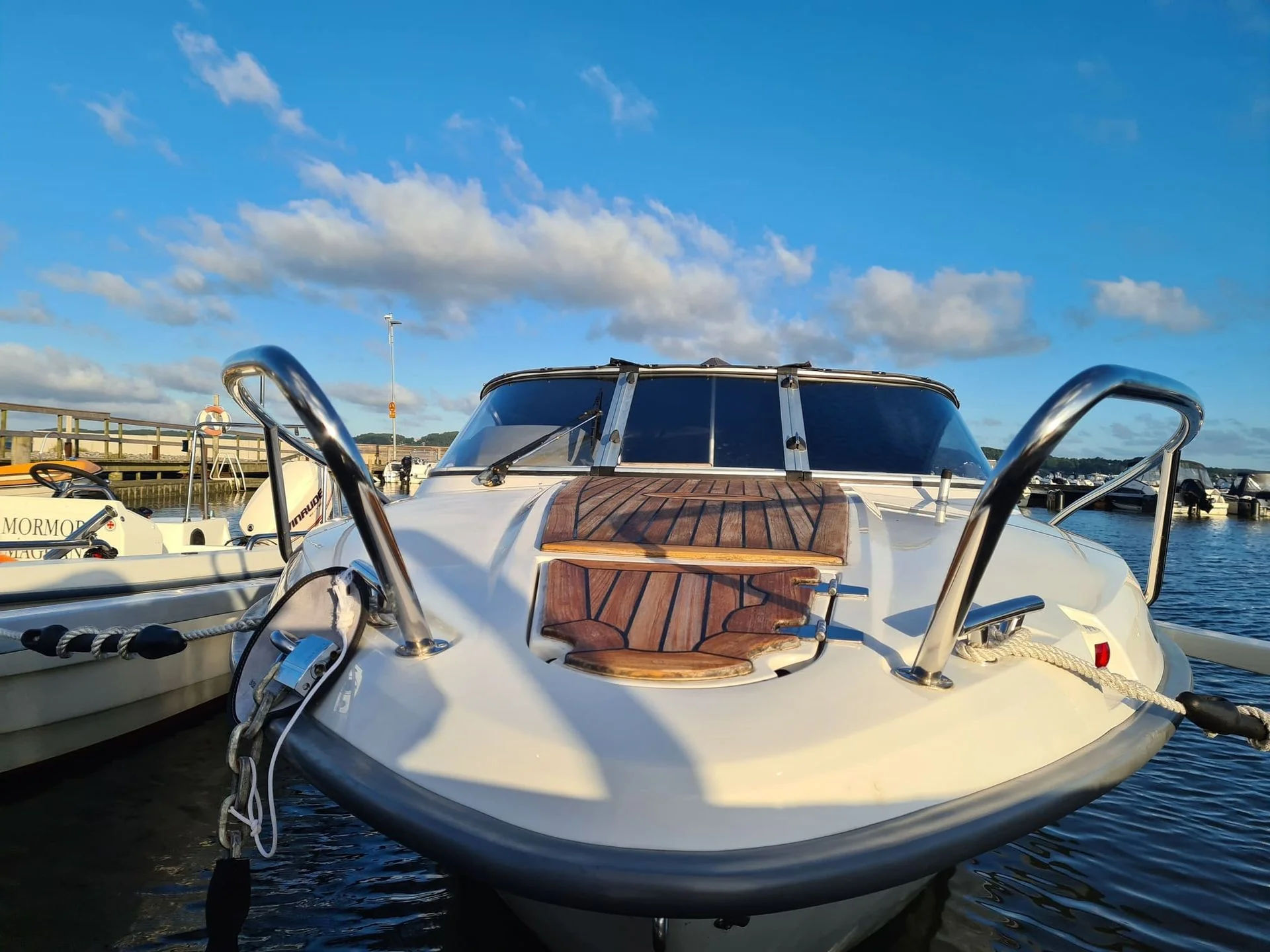 Fiberglass boat with wooden deck seating moored at Jacksonville marina on sunny day.