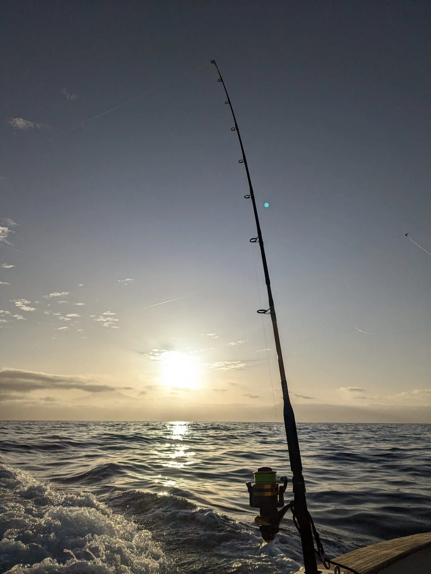 Fishing rod mounted on boat rail against golden-hour ocean horizon and sky.