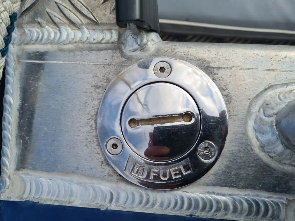 Boat fuel door cap mounted on weathered fiberglass hull showing corrosion and salt spray damage.