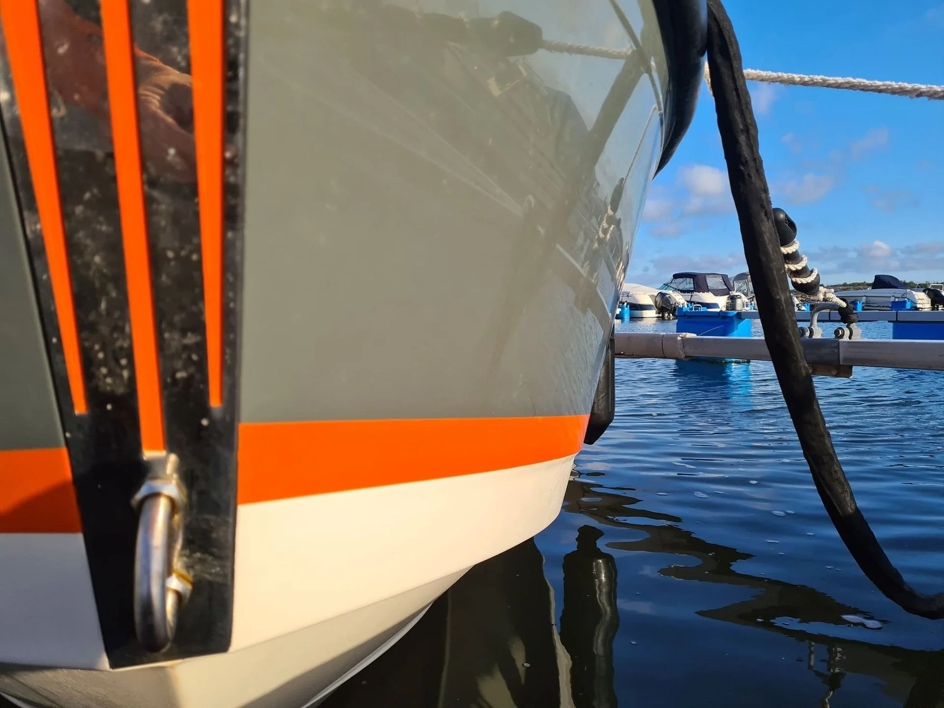 Orange and white boat hull moored at Jacksonville marina with weathered fenders and rope rigging visible.