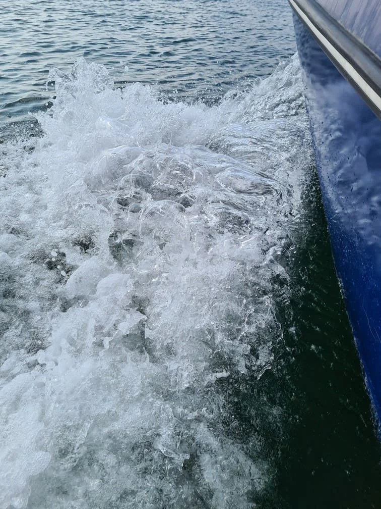 Boat hull edge cutting through foamy wake water during operation.