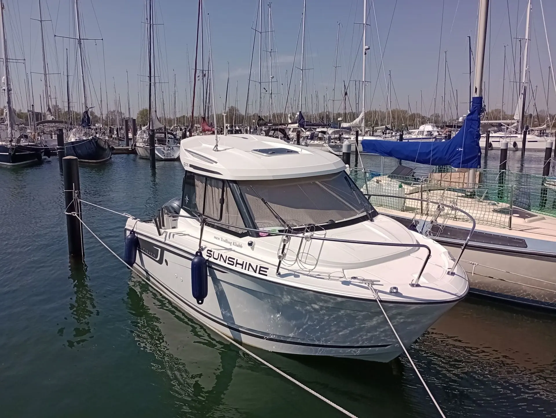 White fiberglass motorboat moored at Jacksonville marina among sailboats on clear day.