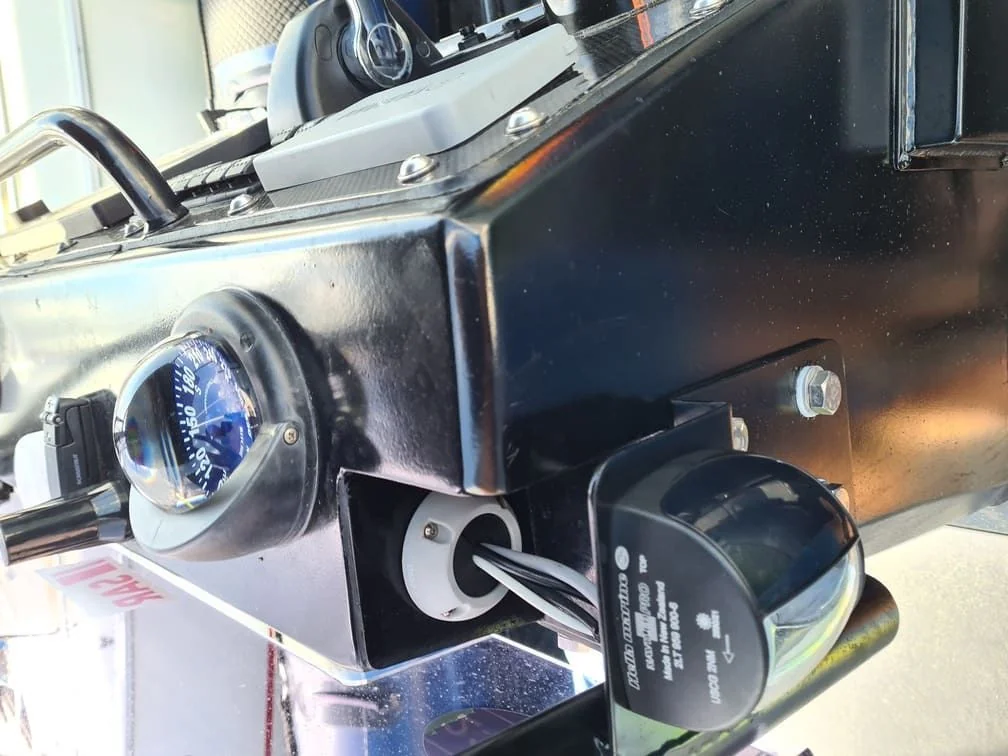 Marine compass and electrical gauge mounted on boat dashboard with salt spray patina.