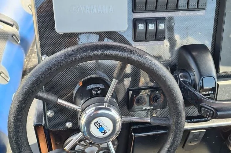 Boat steering wheel and control panel with Yamaha outboard engine gauges visible in bright sunlight.
