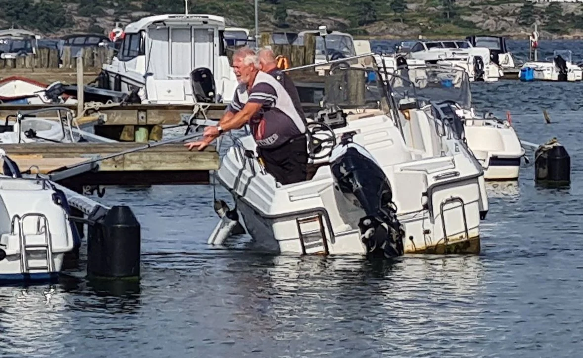 Technician wading in water inspecting outboard motor on white fiberglass boat at Jacksonville marina dock.