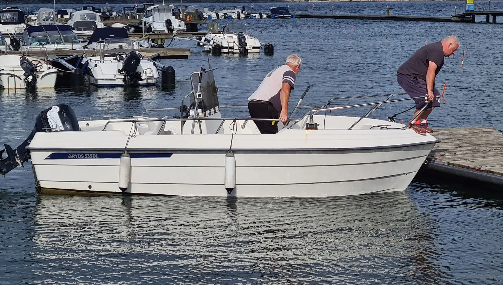 Two men service outboard engine on white fiberglass boat at Jacksonville marina dock.