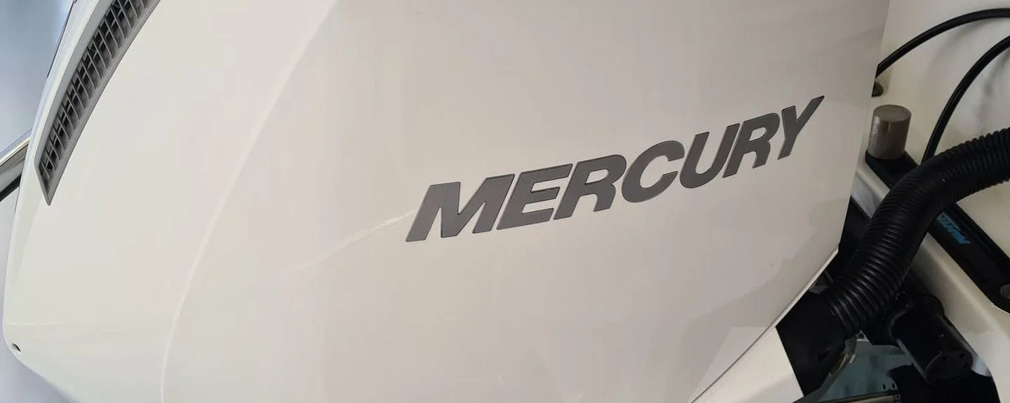 Mercury outboard engine nameplate on white fiberglass boat hull with fuel line visible.